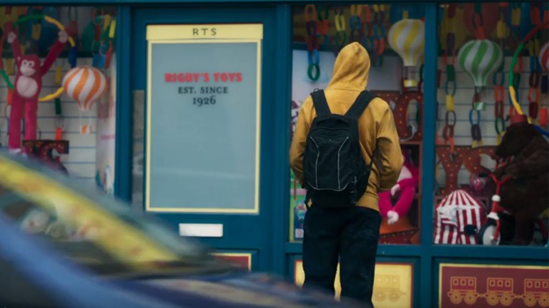 A person wearing a yellow hoodie standing outside of a toy shop - screengrab from The Devil's Hour season 2